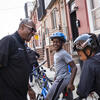 A smiling man in a black shirt with three happy children wearing helmets, sitting on bicycles during a Temple Urban Bike Team practice.