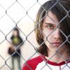 A male teen from the documentary The Bad Kids holding a chain link fence.