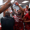 Temple basketball players wearing cherry and white jerseys, smiling brightly douse water on a coach inside the team locker room.