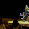 Tina Fey sitting on stage while holding a microphone and laughing.