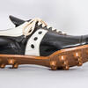 A black and white cleat with a bronze-colored bottom