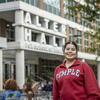 Maria wears a Temple sweatshirt and smiles outside the Liacouras entrance to Alter Hall
