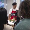 People looking through a camera at students cooking