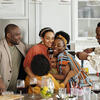 Grandparents, parents and their young children stand around the kitchen smiling and embracing.