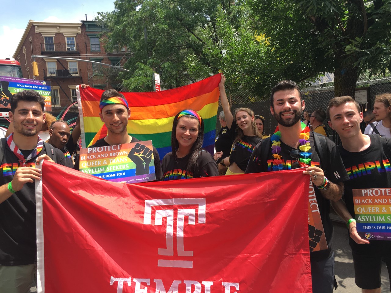 Students and alumni carrying a rainbow Pride flag and a Temple Flag.