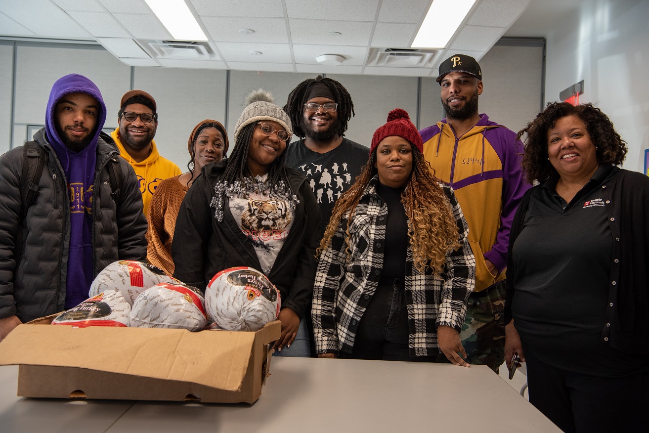 A group of men and women standing in front of a box of turkeys around Thanksgiving at Temple.