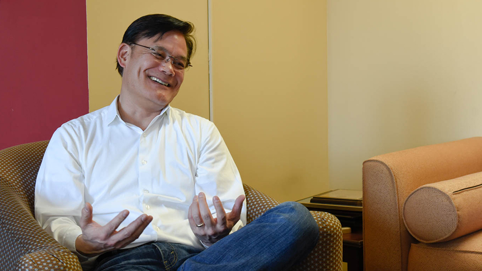 Roger Ideishi smiling and sitting in a chair.